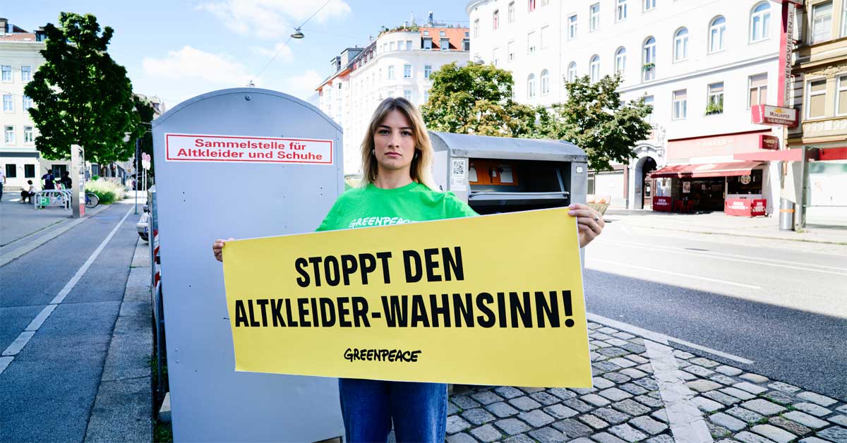 Activist holding a banner reading 'Stoppt den Altkleider Wahnsinn!' (Stop the Used-Clothes Madness!) for Greenpeace campaign.