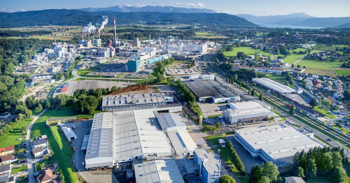 Aerial photo of the Lenzing AG industrial site in Upper Austria with factories, green fields, and mountains in the distance.