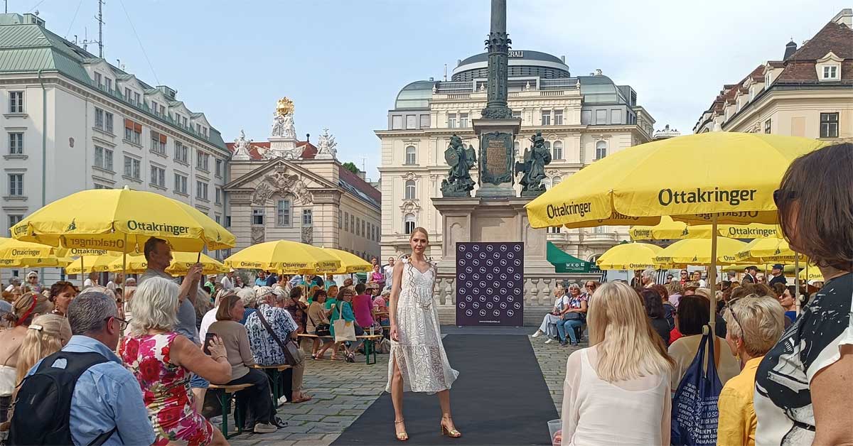 The picture shows the outdoor setting and engaged audience at the Mode Wien fashion show at Am Hof in Vienna, highlighting the community-oriented atmosphere.