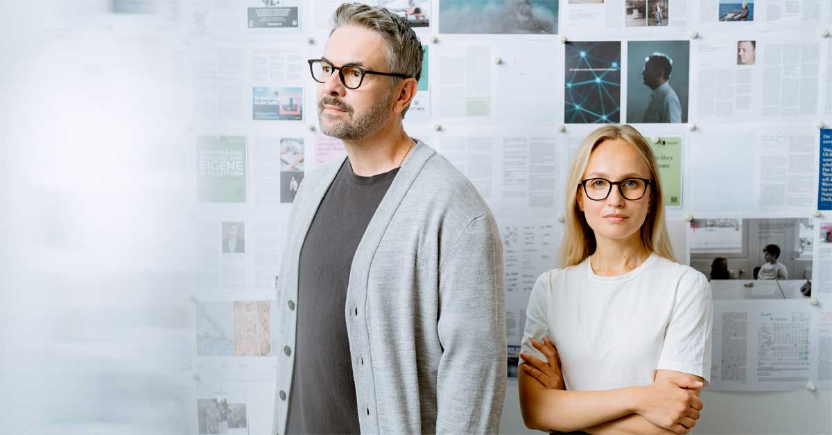 Holger Volland and Olesia Zimmermann in front of a wall with editorial layouts, protagonists of the VIU x brand eins eyewear campaign.