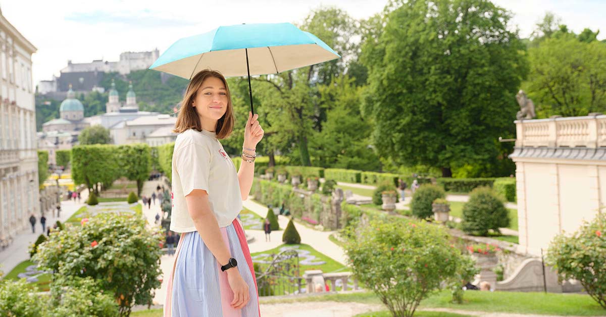 Woman with a UV-protection umbrella overlooking Salzburg's Mirabell Gardens.
