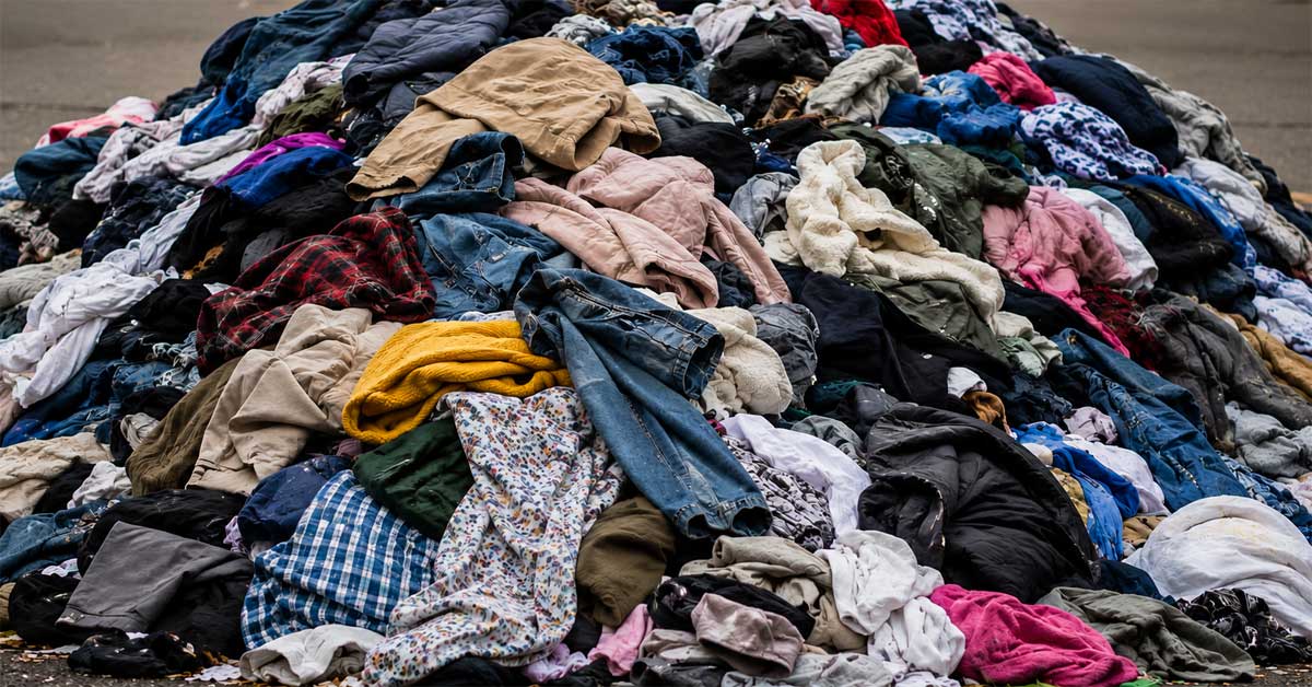 Large pile of used clothing and textiles stacked outdoors, symbolizing textile waste and fast fashion.