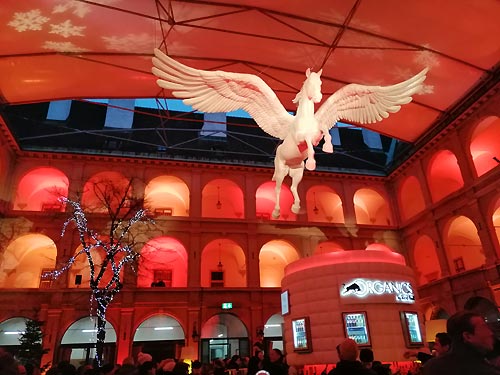 The image shows the sculpture of a flying Pegasus referencing the school's white Lipizzaner horses which are known for performing light-hoofed dance choreographies. The horse stables are visible from the market area. 