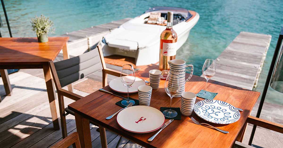 Table set with Gmundner Keramik Navy Blue Flamed and Lobster plates, Marian jug and cups, beside a Marian M800 boat on a lakeside dock.