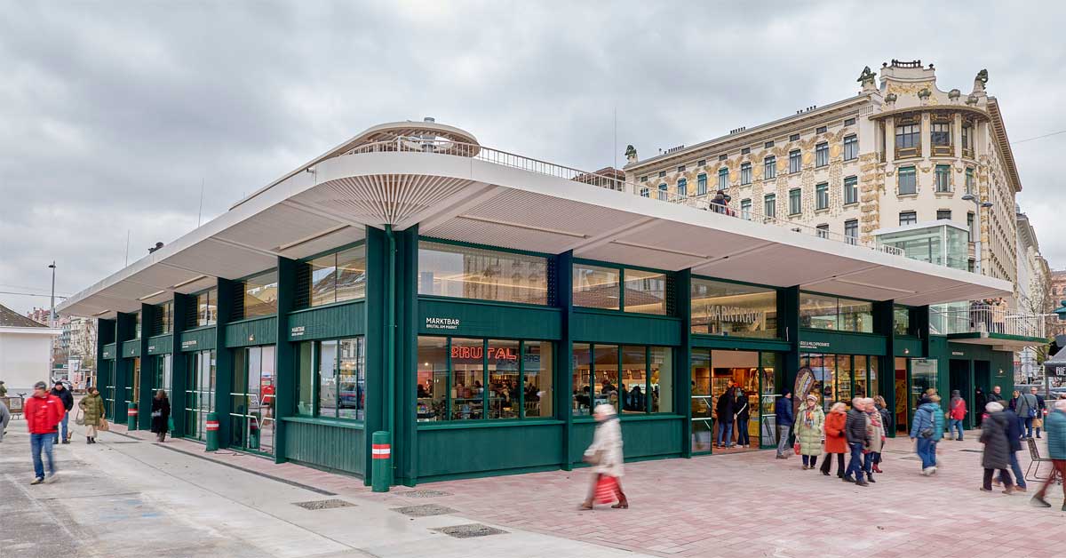 Modern glass-and-wood market hall at Vienna's Naschmarkt with wide roof and people walking in front.