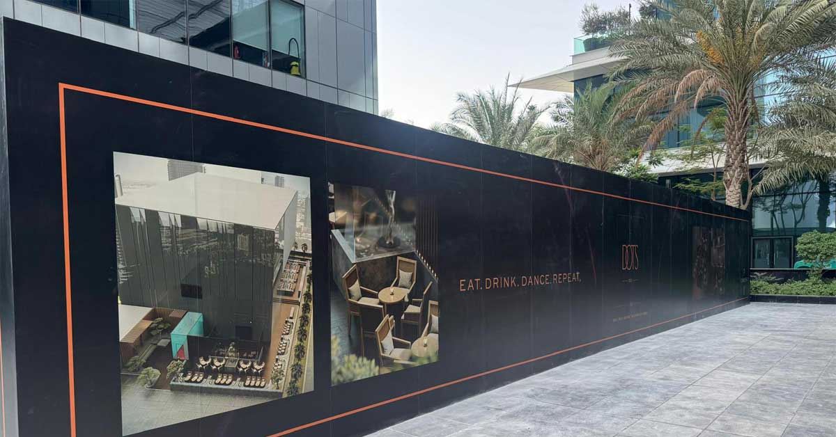 Construction site of DOTS DXB restaurant in Dubai with promotional visuals and brand slogan 'Eat. Drink. Dance. Repeat.' on black facade.