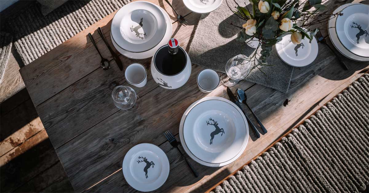 Festive alpine table setting with ceramic plates and deer motif, arranged for a formal dinner.