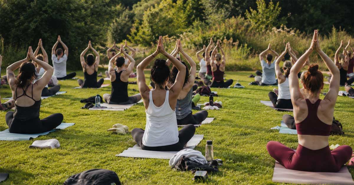 People sitting on a grassy field during an outdoor yoga session in a peaceful summer landscape.