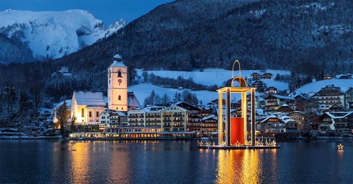 Winter evening at St. Wolfgang with the Peace Light Lantern on Lake Wolfgangsee, surrounded by snowy mountains and festive lights.