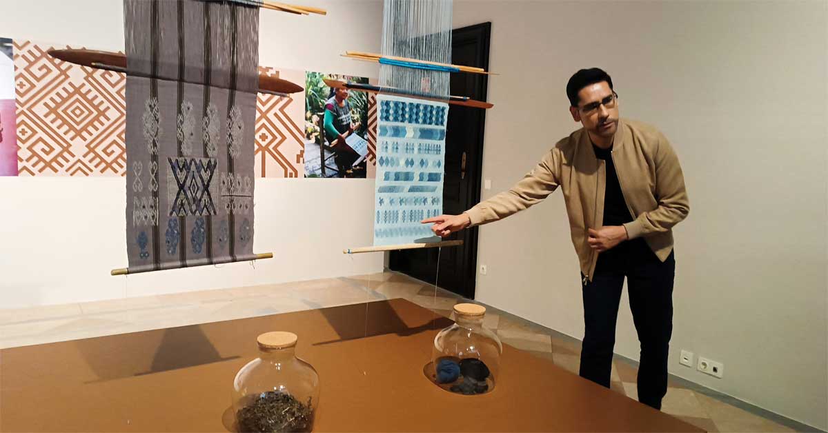 Carlos Barrera Reyes in front of a light blue indigo textile featuring traditional symbols at the Weltmuseum Wien exhibition 'The Colours of the Earth'.