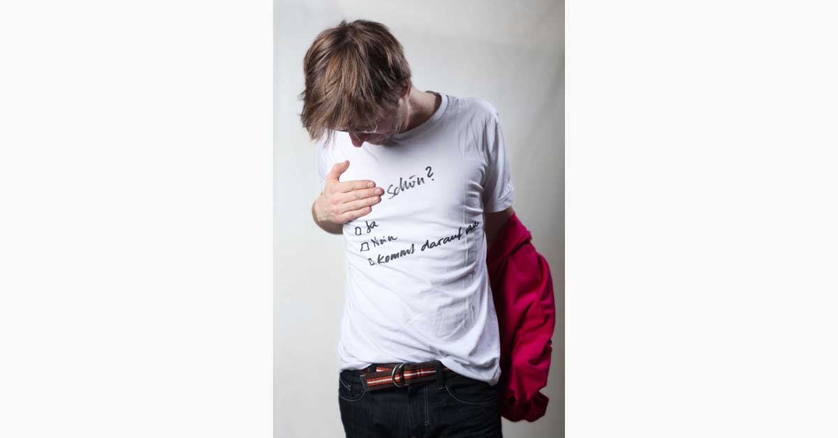 Person looking at a white T-shirt with handwritten 'Schön?' message, illustrating the eSeL Art Swap event and its questions about artistic taste and value.