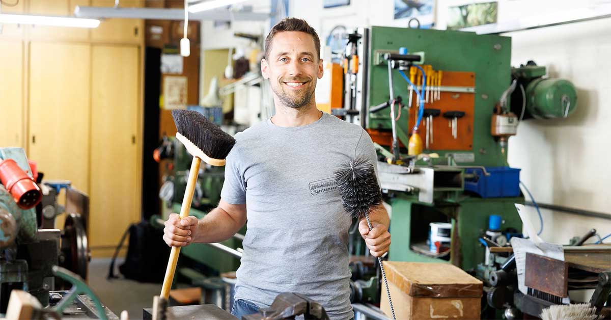 Craftsman holding handmade brushes in a traditional Vienna workshop