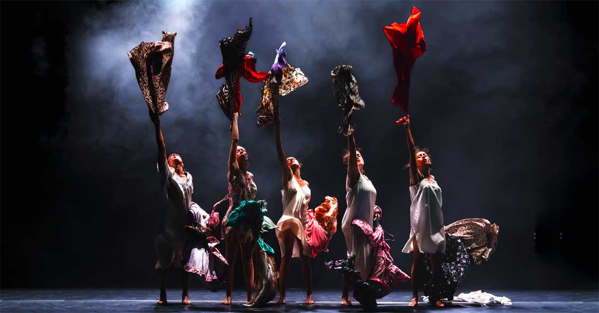 Scene from Leïla Ka's dance performance 'Maldonne' with five dancers holding colourful dresses on stage under dramatic light.