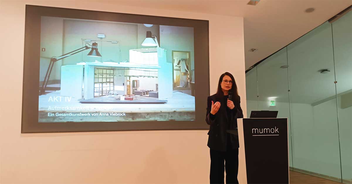 Fatima Hellberg, General Director of mumok, speaking at the 2026 press conference with a projected stage model from 'Terminal Piece' by Anna Viebrock in the background.