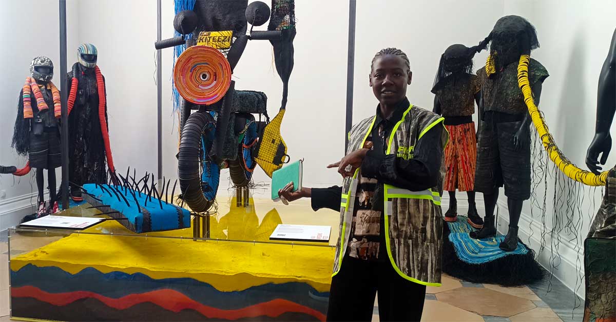Artist Njola standing beside recycled fashion sculptures and a reconstructed Boda Boda installation at the Theseus Temple in Vienna.