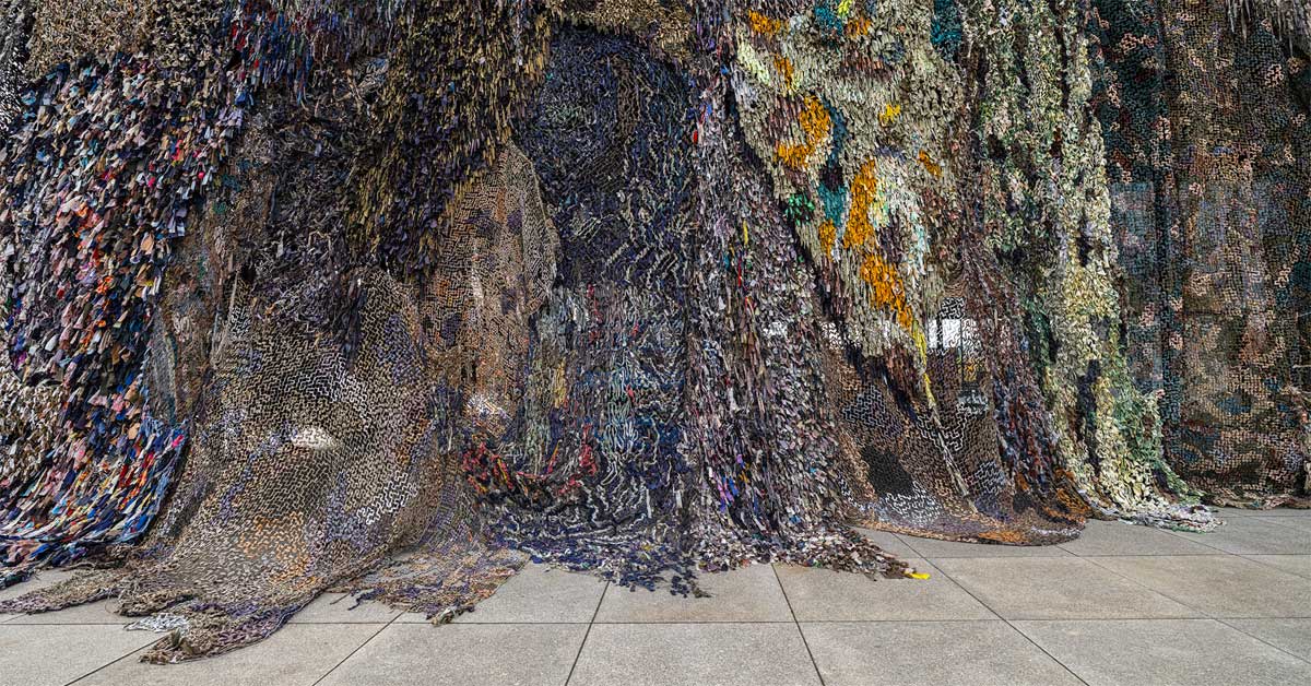 Large camouflage-net installation made from knotted fabric strips.
