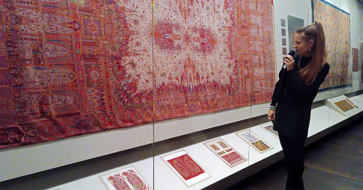 Curator presenting patterned cashmere shawls in a museum exhibition with glass display cases