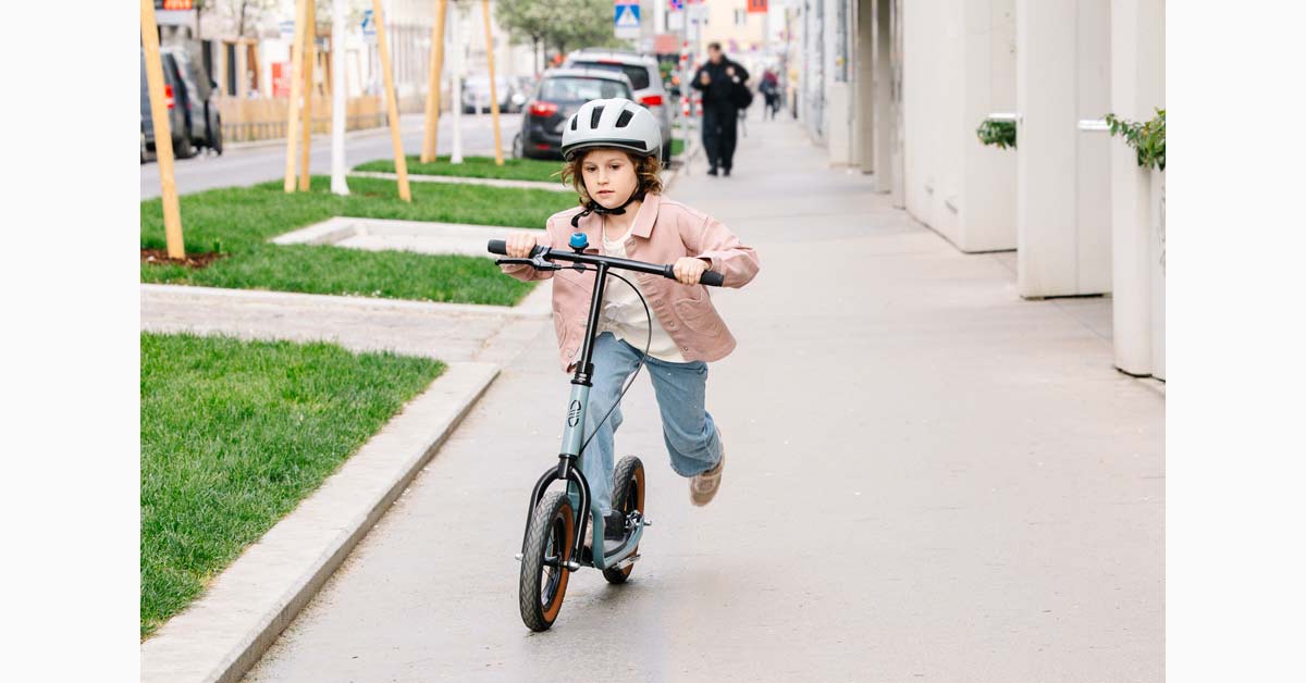Girl wearing a helmet rides a scooter on a city pavement.