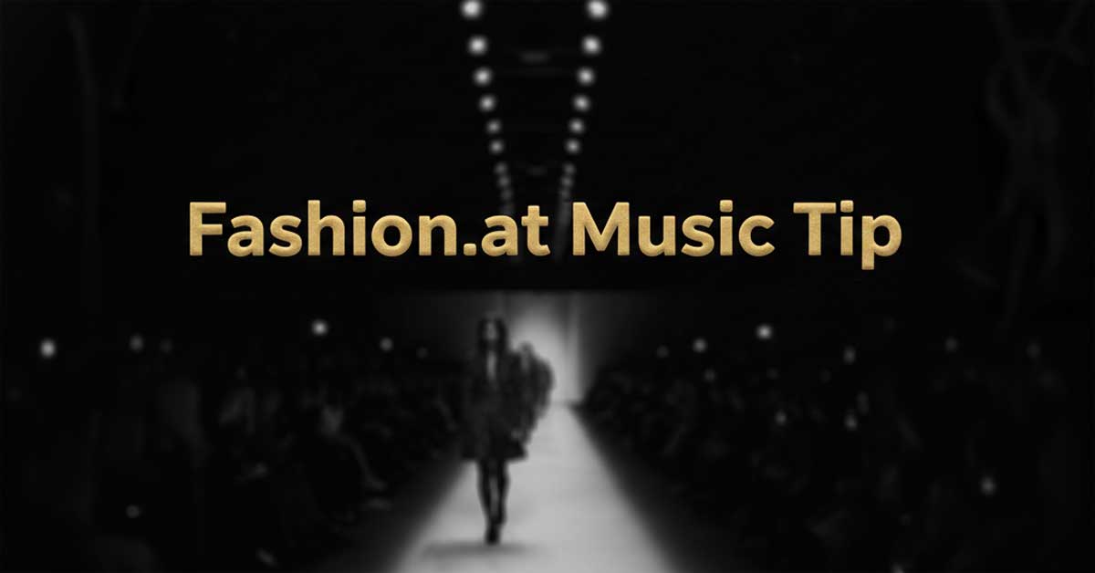 Dark, blurred runway image with 'Fashion.at Music Tip' in gold.