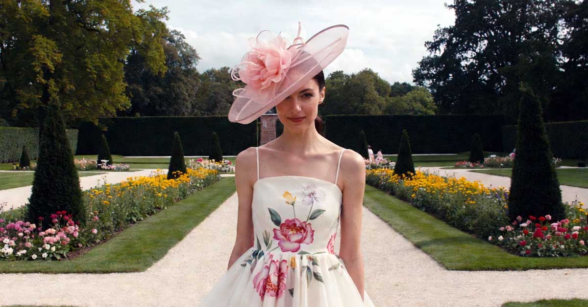 Elegant woman in floral gown and large pink hatinator in a formal garden path